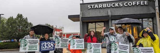 A few Starbucks customers and union allies stand in front of a Starbucks store with signs saying they support Starbucks workers. ta m  